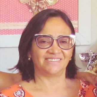 Mulher de cabelos castanhos, óculos e camiseta laranja florida olha para frente