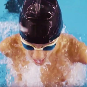 Garoto sem os dois braços está dentro de uma piscina, usando touca e óculos de natação