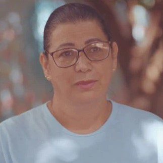 Mulher de cabelos castanhos presos, óculos e camiseta azul olha para frente